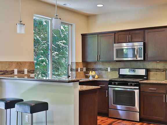 Open, airy kitchen with quartz counters, full-height backsplash, stainless steel appliances, laminate hardwood flooring and counter seating and tranquil east-facing view.