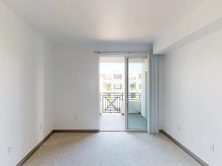 Spacious apartment bedroom with plush carpet flooring and balcony access in select homes.