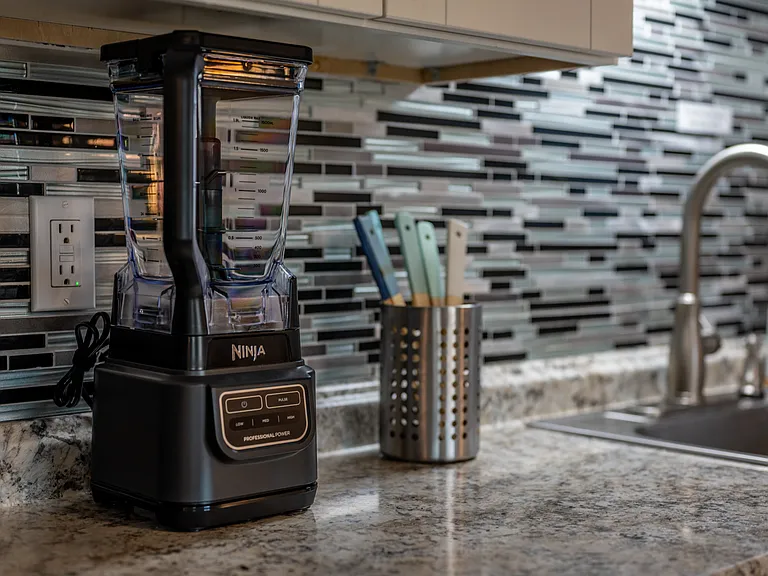 Striped mosaic tile backsplash adds a stylish touch above the sink, while the warm, wood-like flooring complements the clean and inviting aesthetic, making this kitchen perfect for your stay.