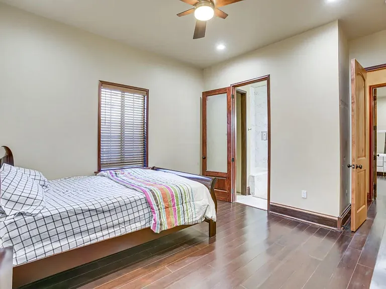 Spacious bedroom with wood-look floors, ceiling fan, and large window with blinds; easy access to adjacent bath/vanity area.