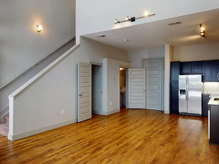 Apartment kitchen with stainless steel appliances, dining and living room with wood-style flooring.