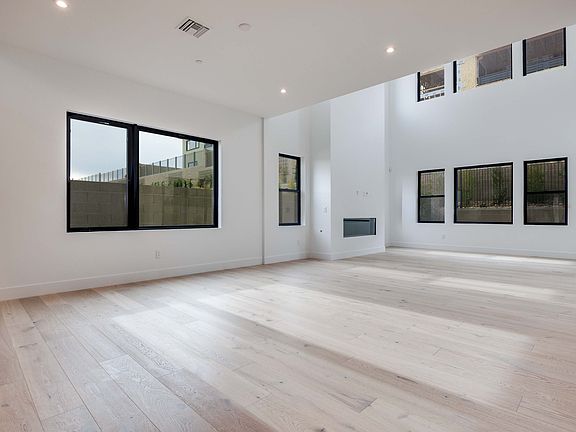 A spacious, minimalist room with large windows, hardwood floors, and framed artwork on the walls.