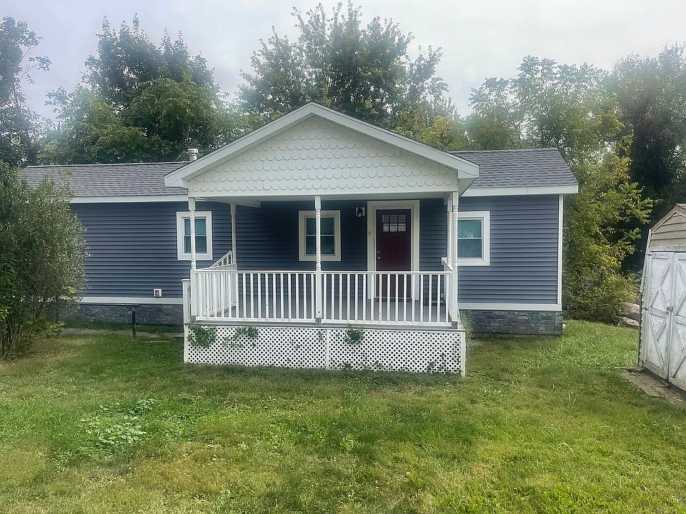 View of front of manufactured home featuring a porch, a front lawn, and a shingled roof