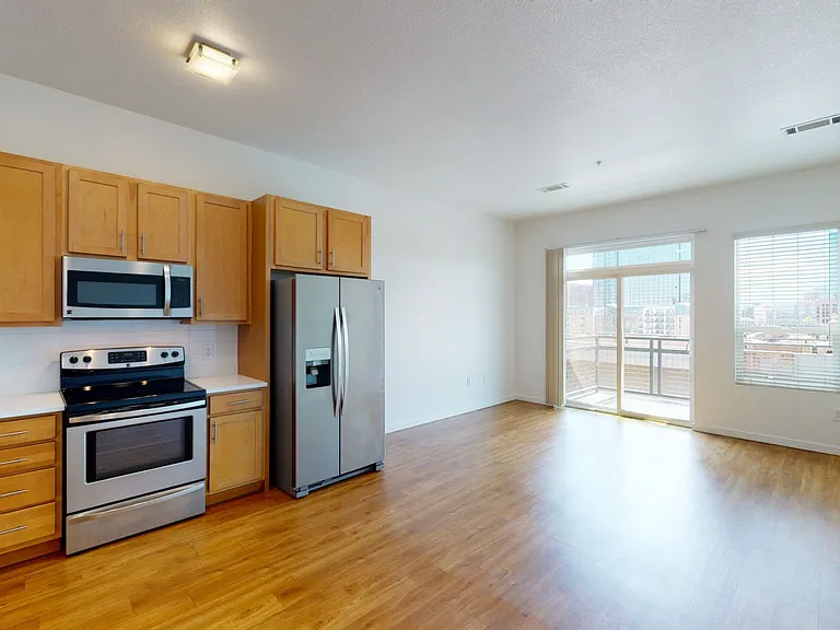 Apartment kitchen with stainless steel appliances, dining and living room with wood-style flooring.