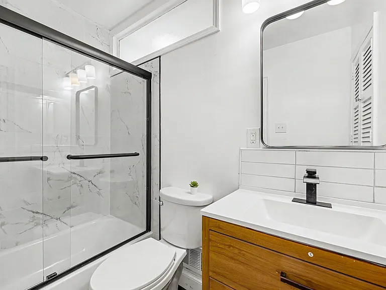 Updated bathroom with a glass-enclosed tub/shower, wide vanity with storage, and a large mirror for daily routines.