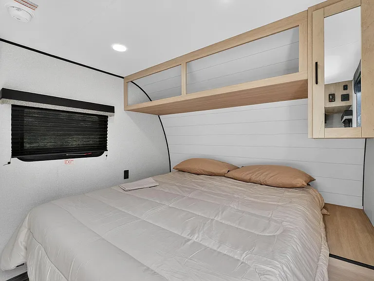 Compact sleeping area with a full bed, overhead storage cabinetry, and a window with privacy shade for comfortable rest.