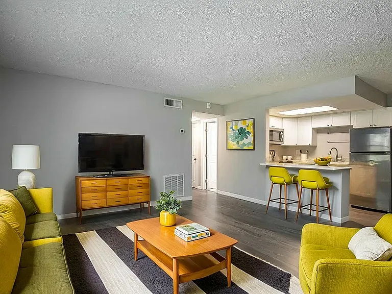 Bright and contemporary living area featuring stylish yellow accents, sleek wood furniture, and an open kitchen with modern appliances.