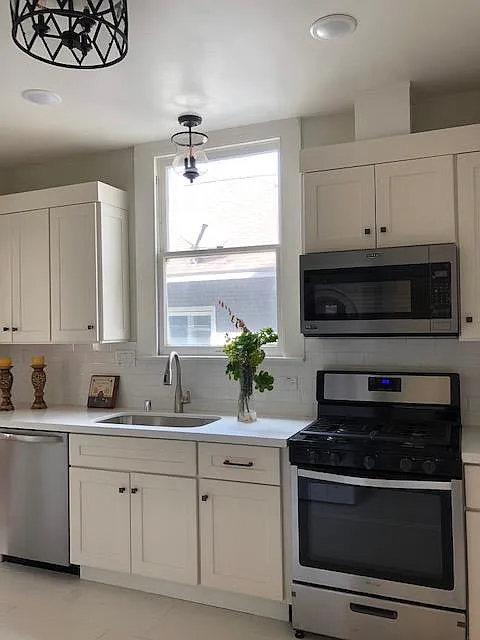 Timeless kitchen with white shaker cabinetry, white subway tile backsplash, tile floors, quartz countertop, stainless steel appliances including gas stove, microwave hood, dishwasher. Ample lighting with natural light through the large window. - 2727 33rd St