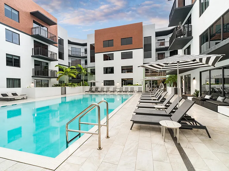 Resort-style pool courtyard with sun loungers, shaded seating, and palm-lined surroundings designed for outdoor relaxation and social connection.