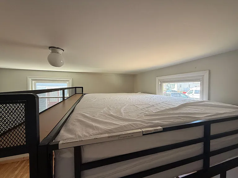 Sleeping area with a bunk bed setup, overhead lighting, and two windows offering neighborhood views and daylight.