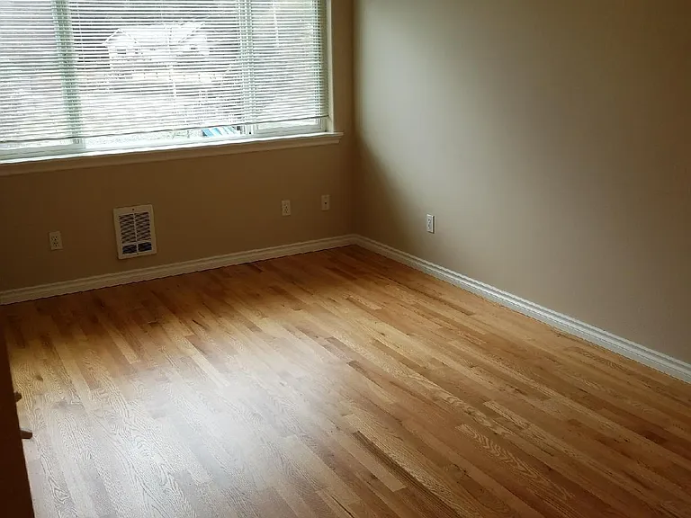 Hardwood floors in living room with large light and bright window.