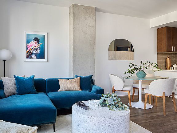 Apartment kitchen with stainless steel appliances, dining and living room with wood-style flooring.