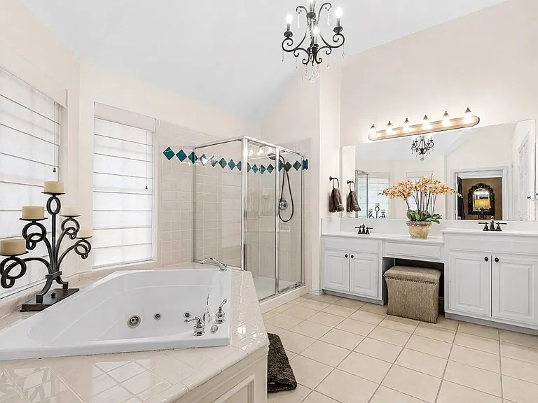 Spacious bathroom featuring a corner soaking tub, glass-enclosed shower, dual vanity with white cabinetry, and ceramic tile flooring