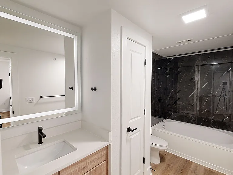 Apartment bathroom with large soaking tub, wood-style flooring and LED vanity mirror.