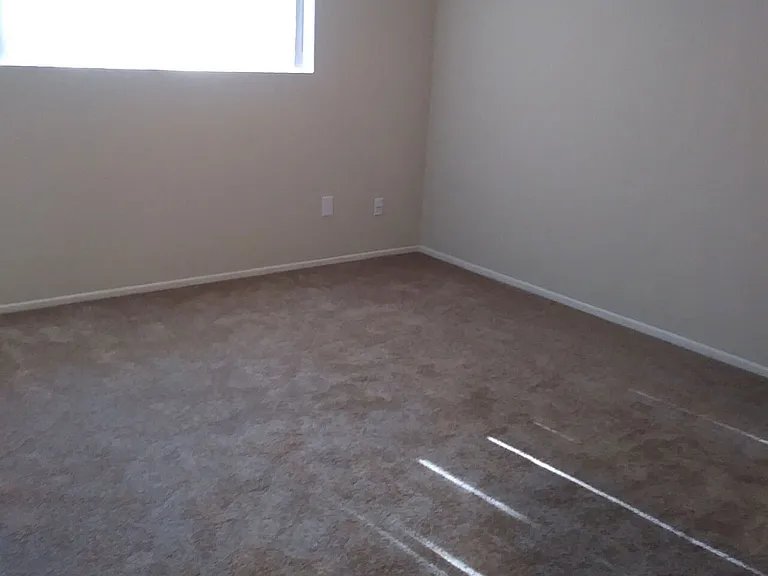 Carpeted bedroom with large window at Teton Pines Apartments in Escondido, California.