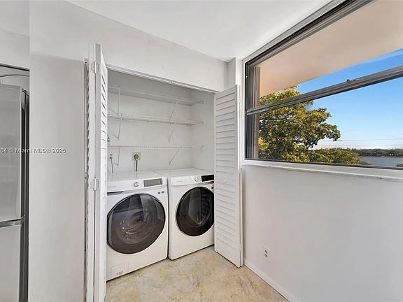 New Samsung washer and dryer in laundry area in kitchen. Storage shelving above washer and dryer. Bi-fold doors make for a neat appearance.