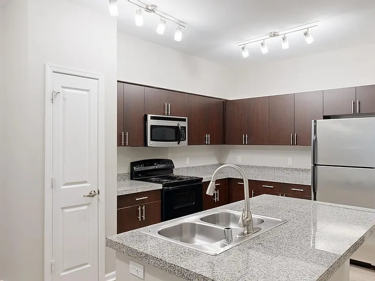 Apartment kitchen with stainless steel appliances, granite countertops, and wood-style flooring.