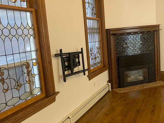 living room with working gas fireplace; between 2 windows a black mounting bracket for TV