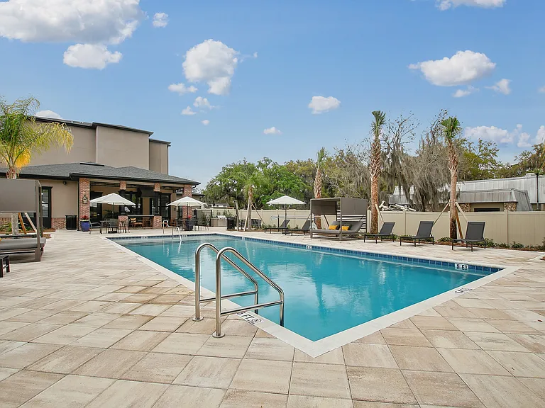 Luxurious outdoor pool area surrounded by elegant lounge chairs and lush palm trees, offering a serene escape with clear blue skies.