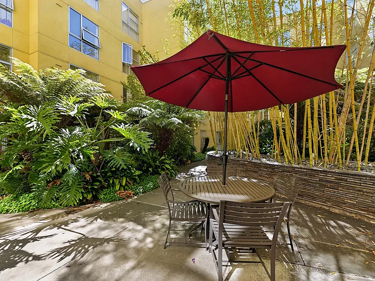 Courtyard seating area with umbrella table, bamboo, and lush landscaping.