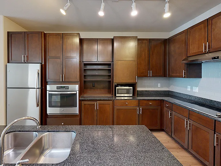 Apartment kitchen with stainless steel appliances, granite countertops and wood-style flooring.
