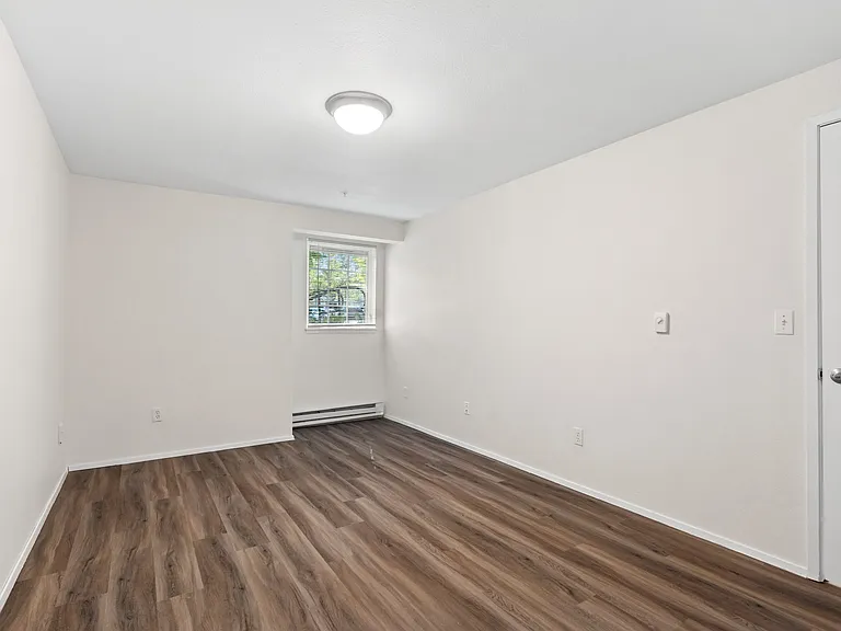 Spacious bedroom with wood-style flooring, neutral finishes, and natural light.