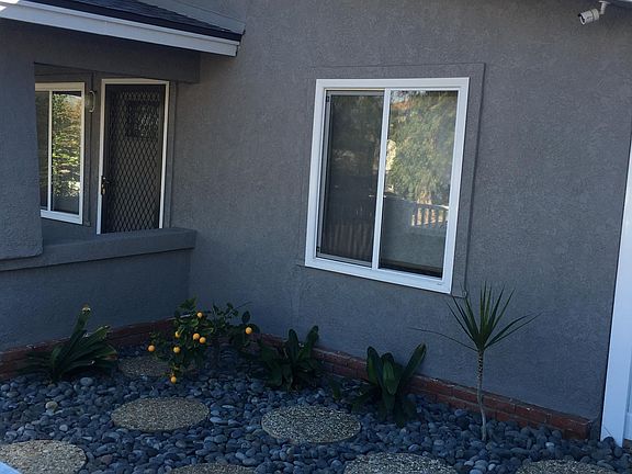 Front of House. Rock and pavers, fruit trees. White vinyl fencing and gates.