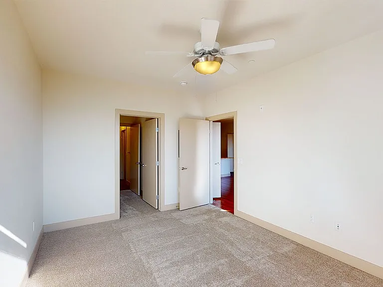 Spacious apartment bedroom with large closet, attached bathroom and plush carpet flooring.
