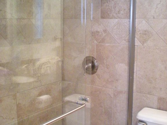 Travertine tiled shower with glass shower doors. Travertine floor.