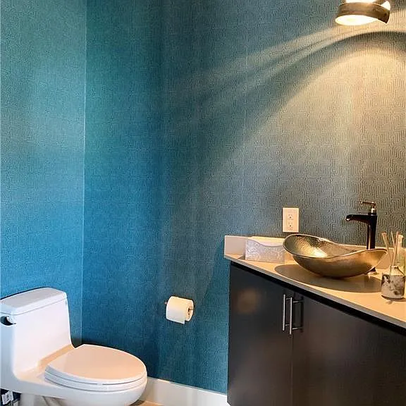 This designer powder room features elegant textured wallpaper, a hammered metal vessel sink, sleek cabinetry, and modern lighting, creating a sophisticated and inviting space for guests.