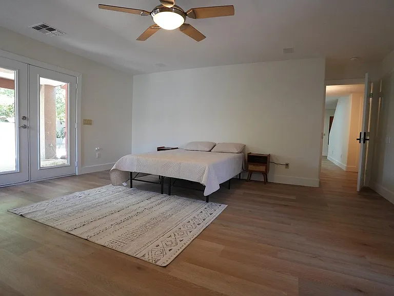 Spacious bedroom with wood-style flooring, ceiling fan, and large glass doors providing easy outdoor access.