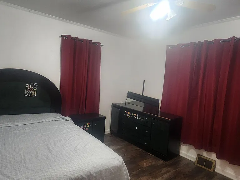 Spacious bedroom with a full bed, coordinating nightstand and dresser, plus two windows with blackout-style curtains.