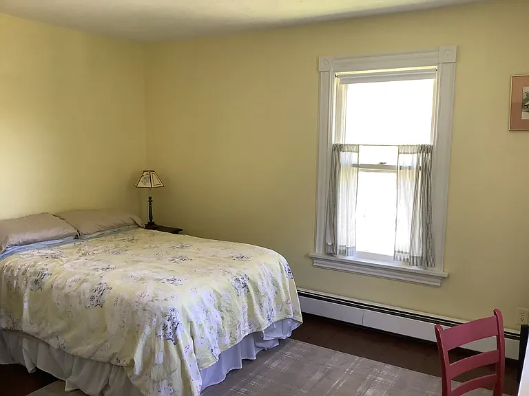 Bedroom 1, overlooks back yard foliage. Floors are painted wood with area rugs,