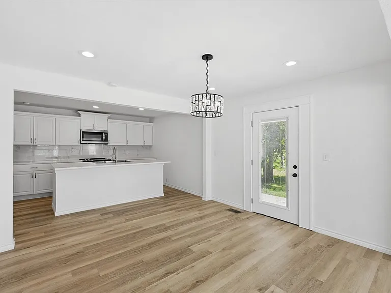 Kitchen with stainless steel microwave, light wood-style floors, light countertops, decorative backsplash, and white cabinets