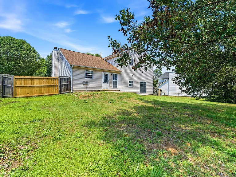 Spacious fenced backyard with a grassy lawn and mature trees, offering room to relax or entertain outdoors.