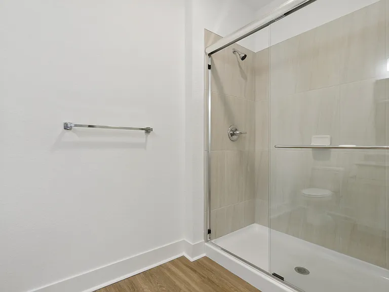 Elegant bathroom featuring a sleek glass shower, modern fixtures, and polished wood flooring, offering a luxurious and serene atmosphere.