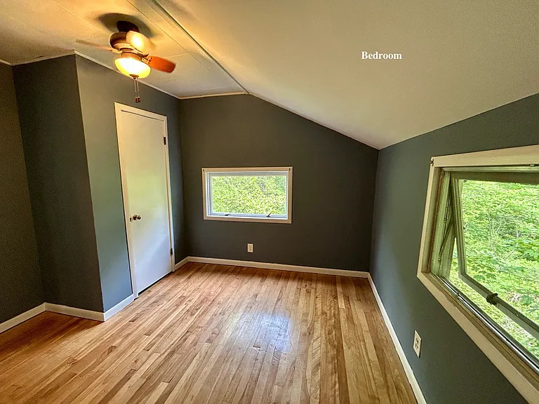 Bedroom with ceiling fan and windows to surounding wooded area
