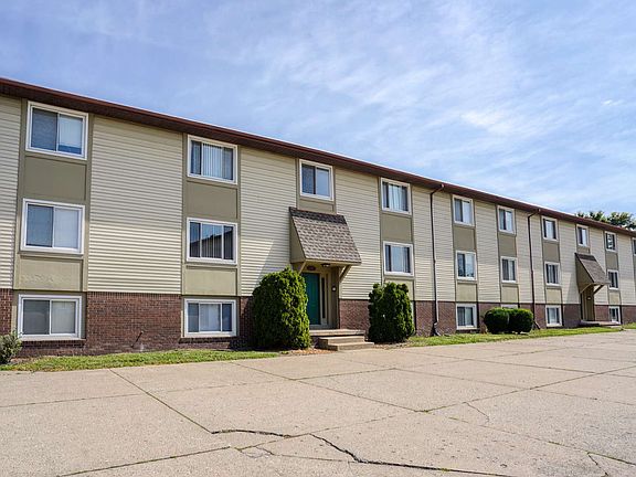 A three-story apartment building with grassy area, and clear blue sky.