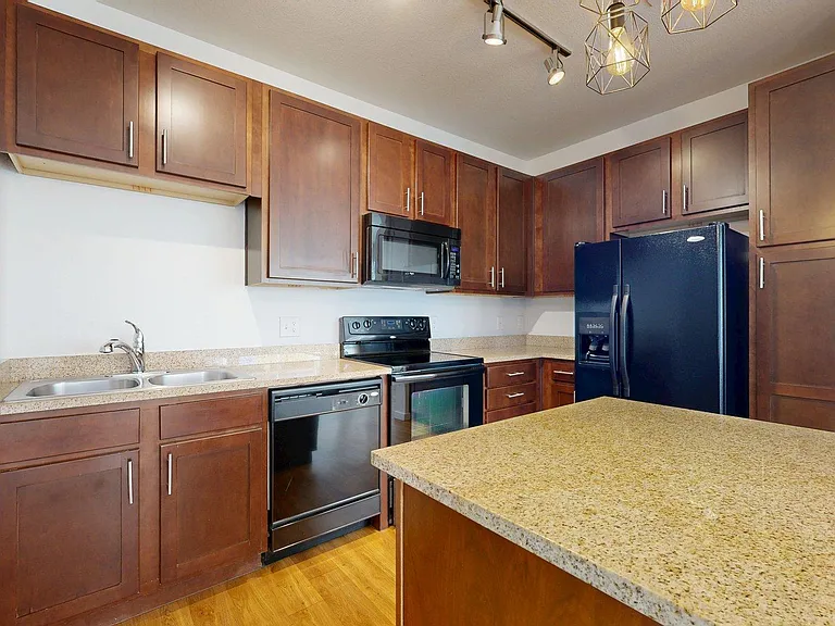 Apartment kitchen with granite countertops and wood-style flooring.