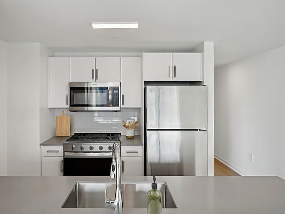 Renovated Package I kitchen with stainless steel appliances, white cabinetry, tile backsplash, grey quartz countertops, and hard-surface flooring