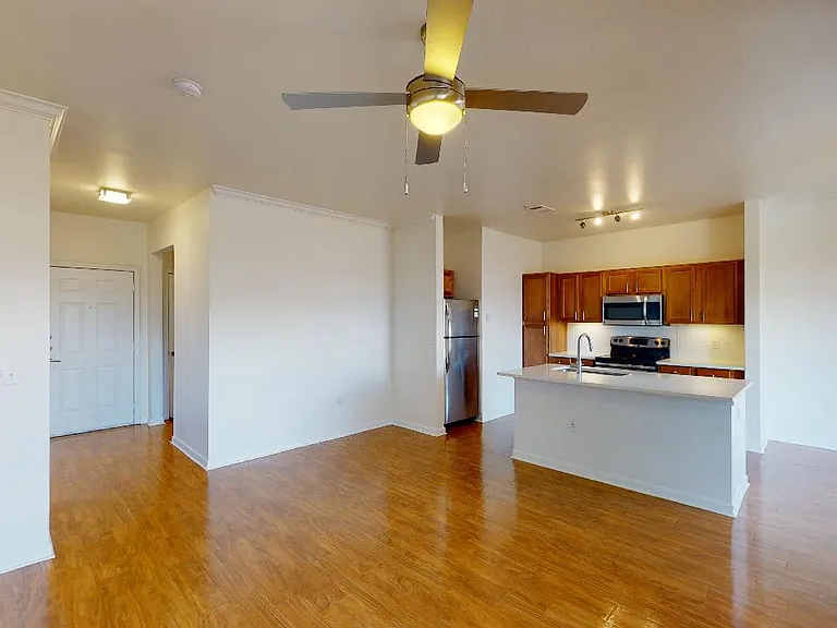 Apartment kitchen with stainless steel appliances and wood-style flooring. Quartz-style countertops (shown here) are available in select homes.