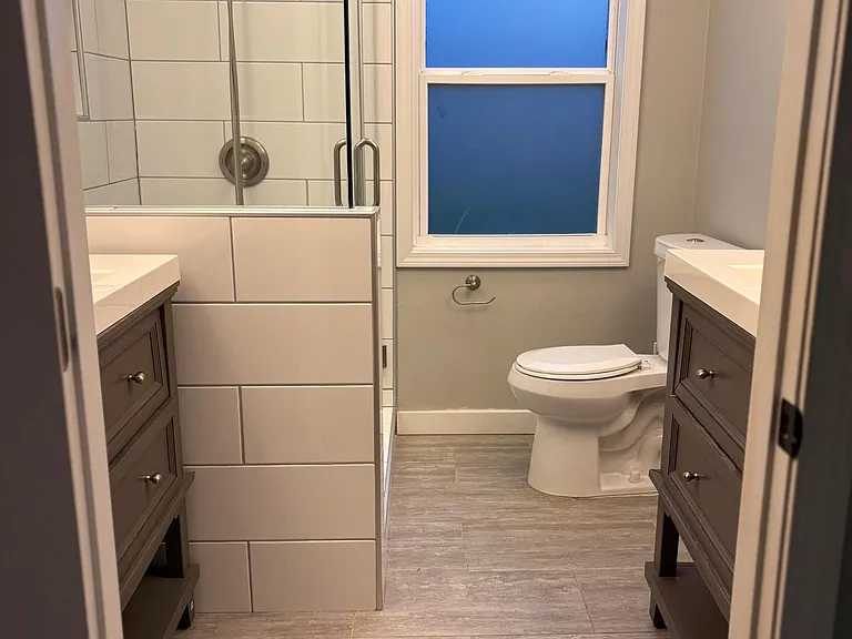 Updated full bath with tiled walk-in shower, dual vanities, and a frosted window for privacy and natural light.