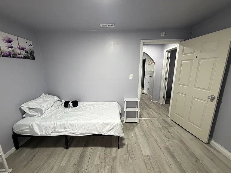 Furnished private bedroom with wood-look flooring, neutral walls, and space for a nightstand or small dresser.