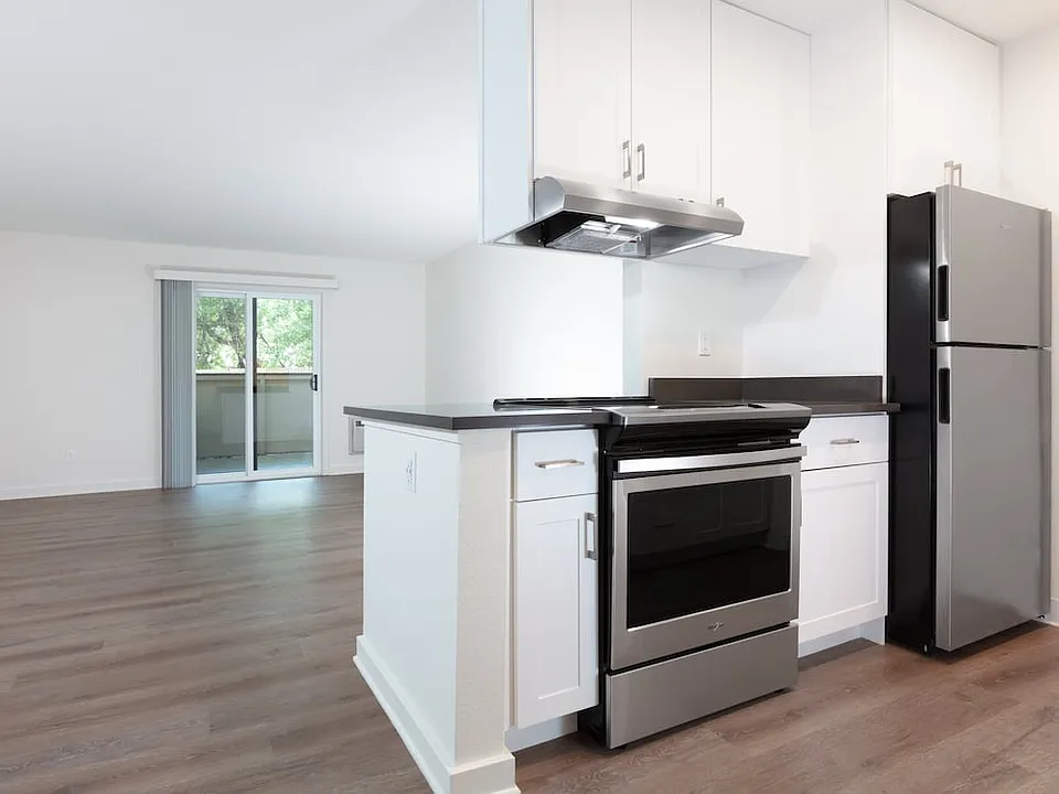Living area with balcony access and kitchen with white cabinetry, dark grey countertops, stainless steel appliances and hard surface flooring