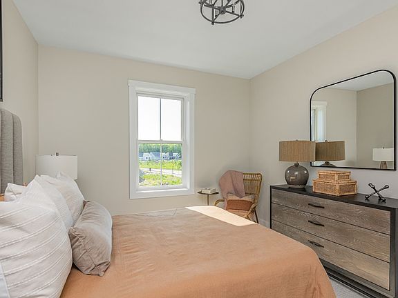 Modern bedroom with a large bed, grey headboard, dresser with mirror, side table, and a window showi