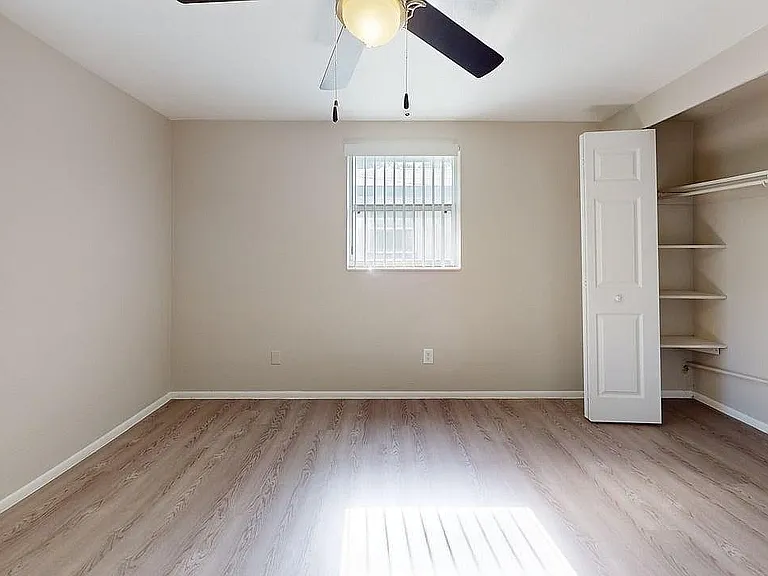 Bright and airy bedroom with elegant hardwood floors, ceiling fan, open closet, and charming window view.