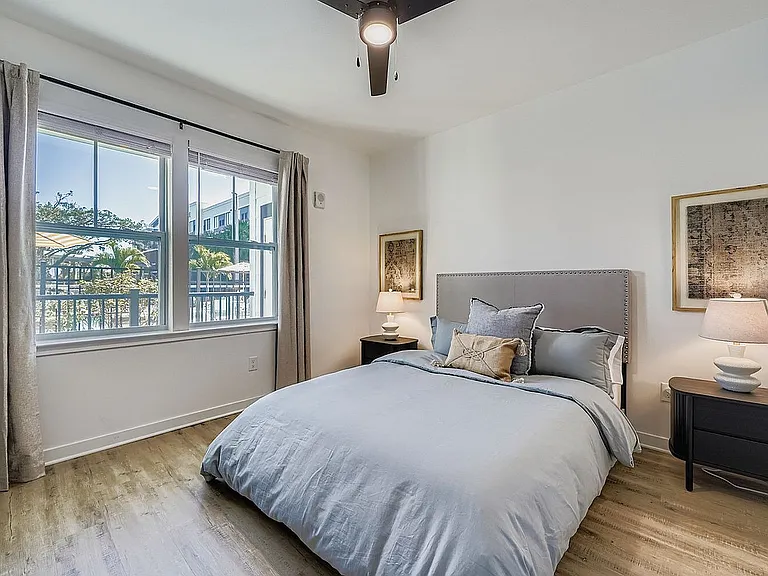 Inviting bedroom with contemporary decor, featuring a large window with a lush outdoor view, a plush bed with elegant pillows, and warm ambient lighting.