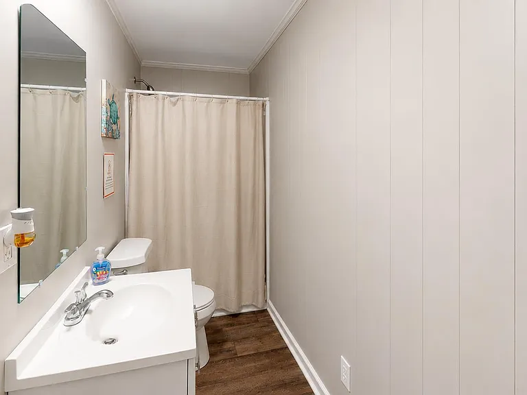 Streamlined full bath with vanity and mirror, wood-look flooring, and a tub/shower combo with curtain for easy upkeep.