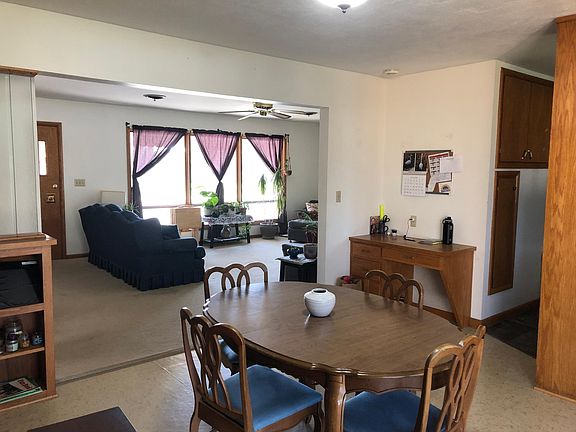 Dining room looking from deck doors towards the living room and front door. Kitchen is to the right. Desk and built in storage cabinets by the kitchen entrance. Built in shelves on the left
