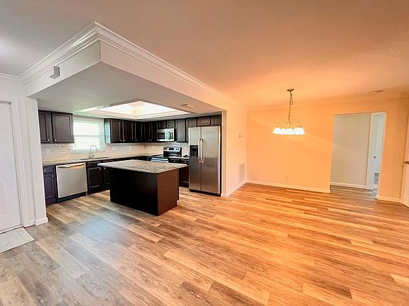 View of kitchen from fireplace. and 
Front door entry is at far left in photo. 
Dining area is just right of center under the chandelier with the hallway that goes into the primary bedroom off to the right and guest bedroom off to left. Guest bath sep